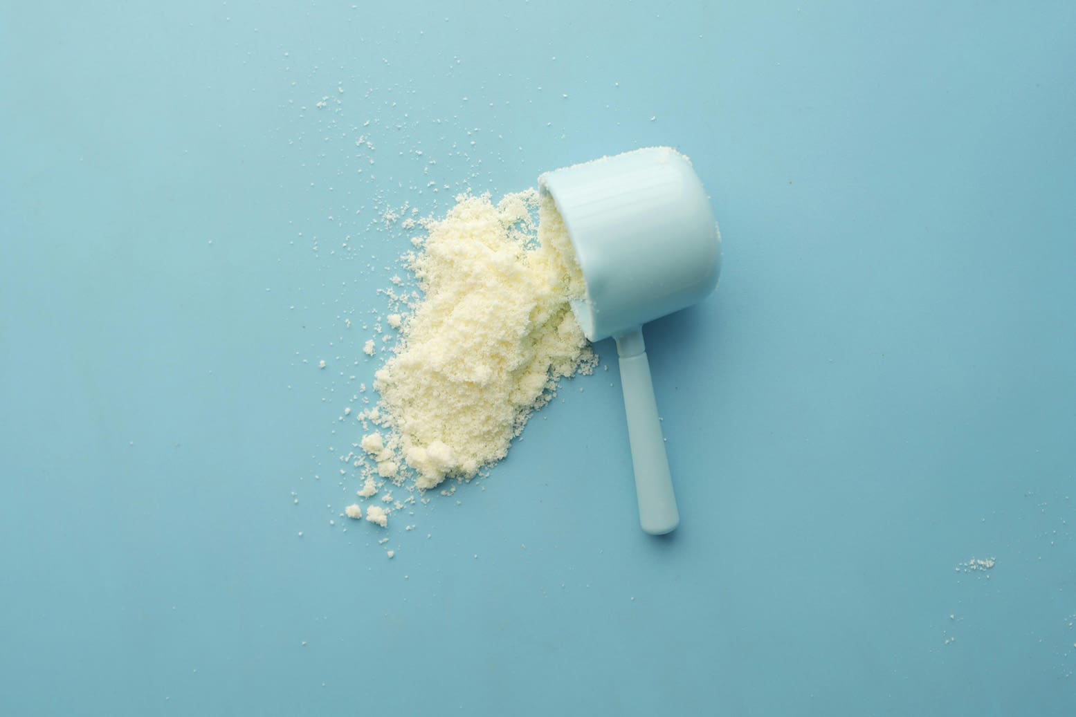 Creatine supplement powder falling out of a measuring cup against a blue background
