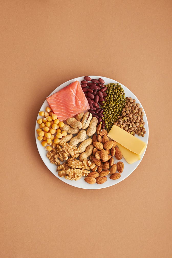 Bowl of healthy fat options on a plate against a peach colored backdrop.